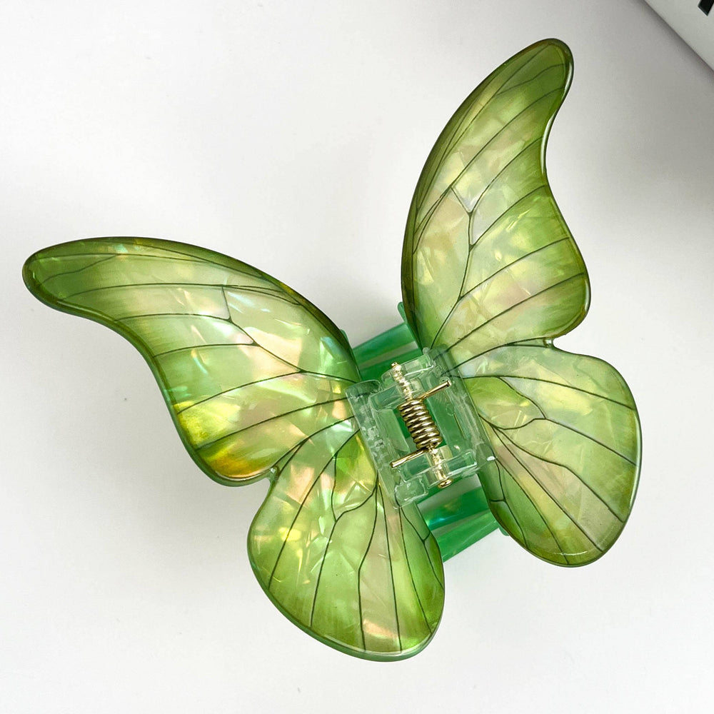 Green butterfly-shaped hair clip on a white background with a plant in the corner.